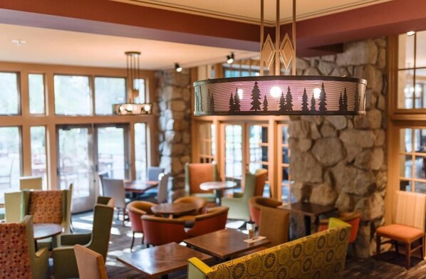 A restaurant with a stone wall, large windows, and various seating arrangements including tables and chairs. - The Ahwahnee (Yosemite National Park)