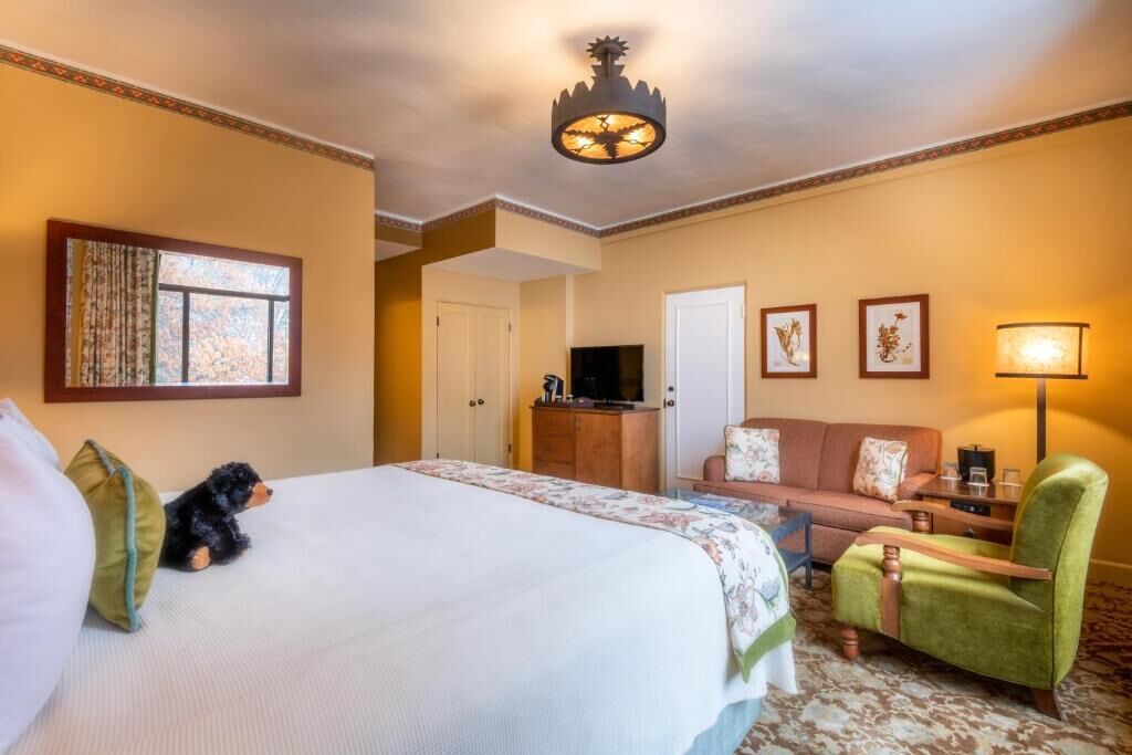 Une chambre d’hôtel avec un grand lit, un fauteuil vert, un canapé, une télévision et une lampe.