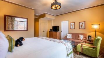 Une chambre d’hôtel avec un grand lit, un fauteuil vert, un canapé, une télévision et une lampe.