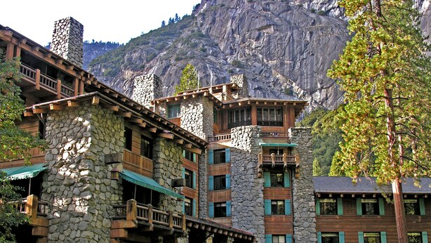 A multi-story stone building with balconies and outdoor seating areas, set against a mountainous backdrop.