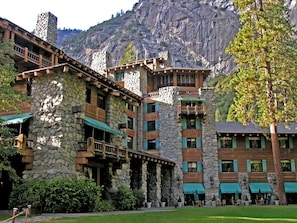 A multi-story stone building with balconies and outdoor seating areas, set against a mountainous backdrop. - The Ahwahnee (Yosemite National Park)