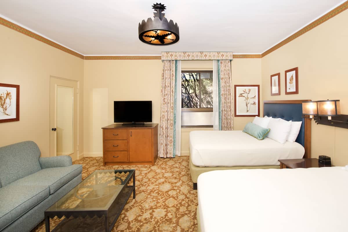 Een hotelkamer met een bed, een bank, een televisie, een bureau en een raam met gordijnen.