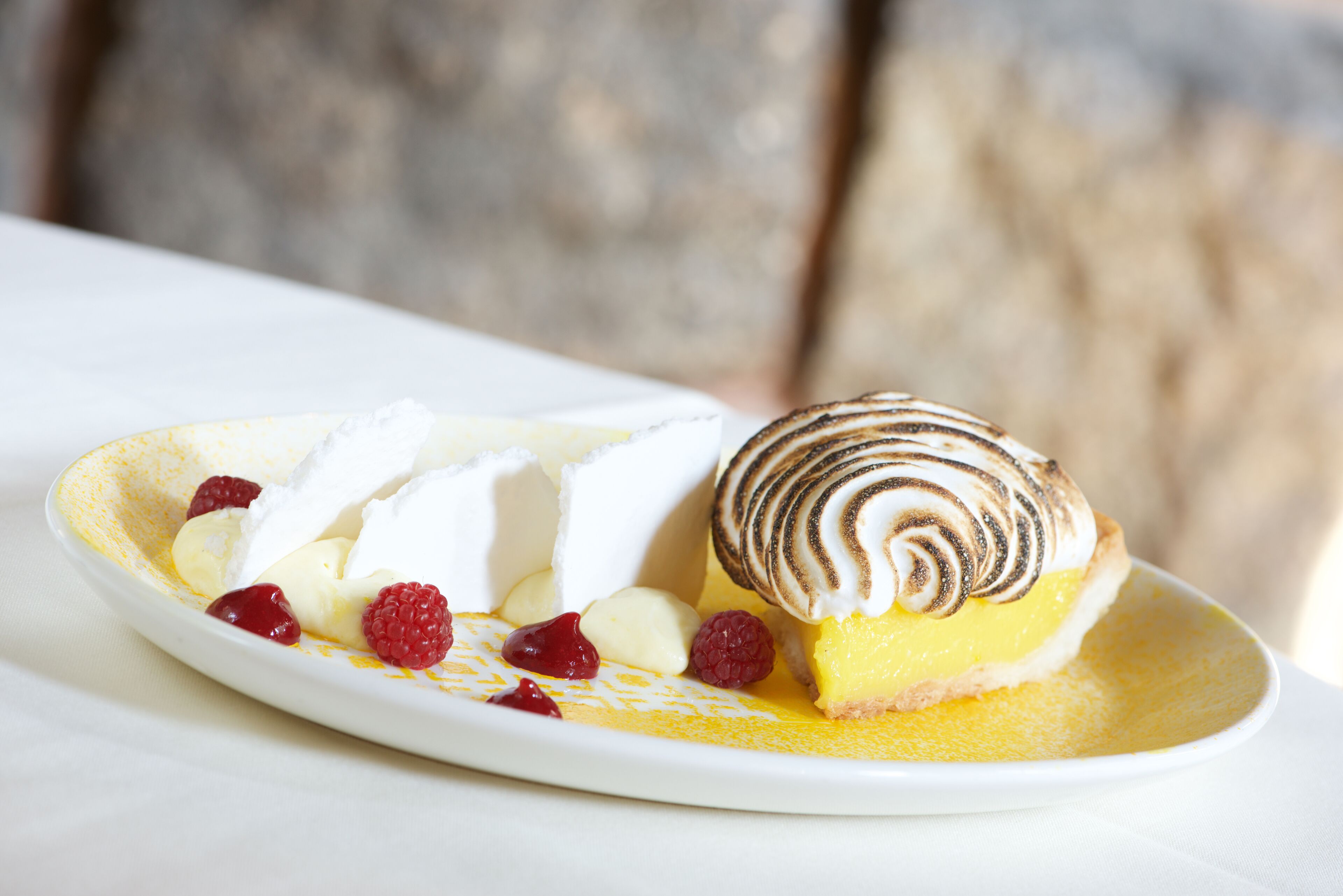 Un plato de postre con merengue, crema y frambuesas.