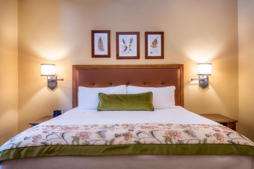 Een hotelkamer met een groot bed, bloemenbeddengoed, een groen kussen en ingelijste botanische kunst aan de muur.