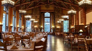 A spacious dining hall with high ceilings and chandeliers, featuring multiple tables and chairs arranged for dining.