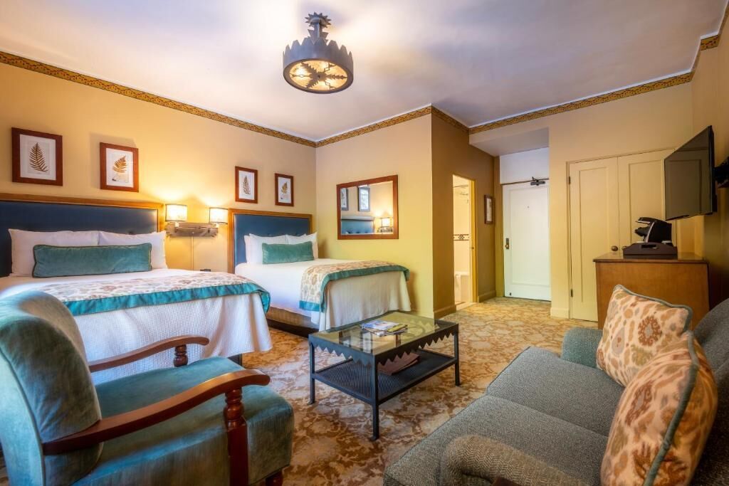 A hotel room with two beds, a sofa, a chair, a small table, and a television.