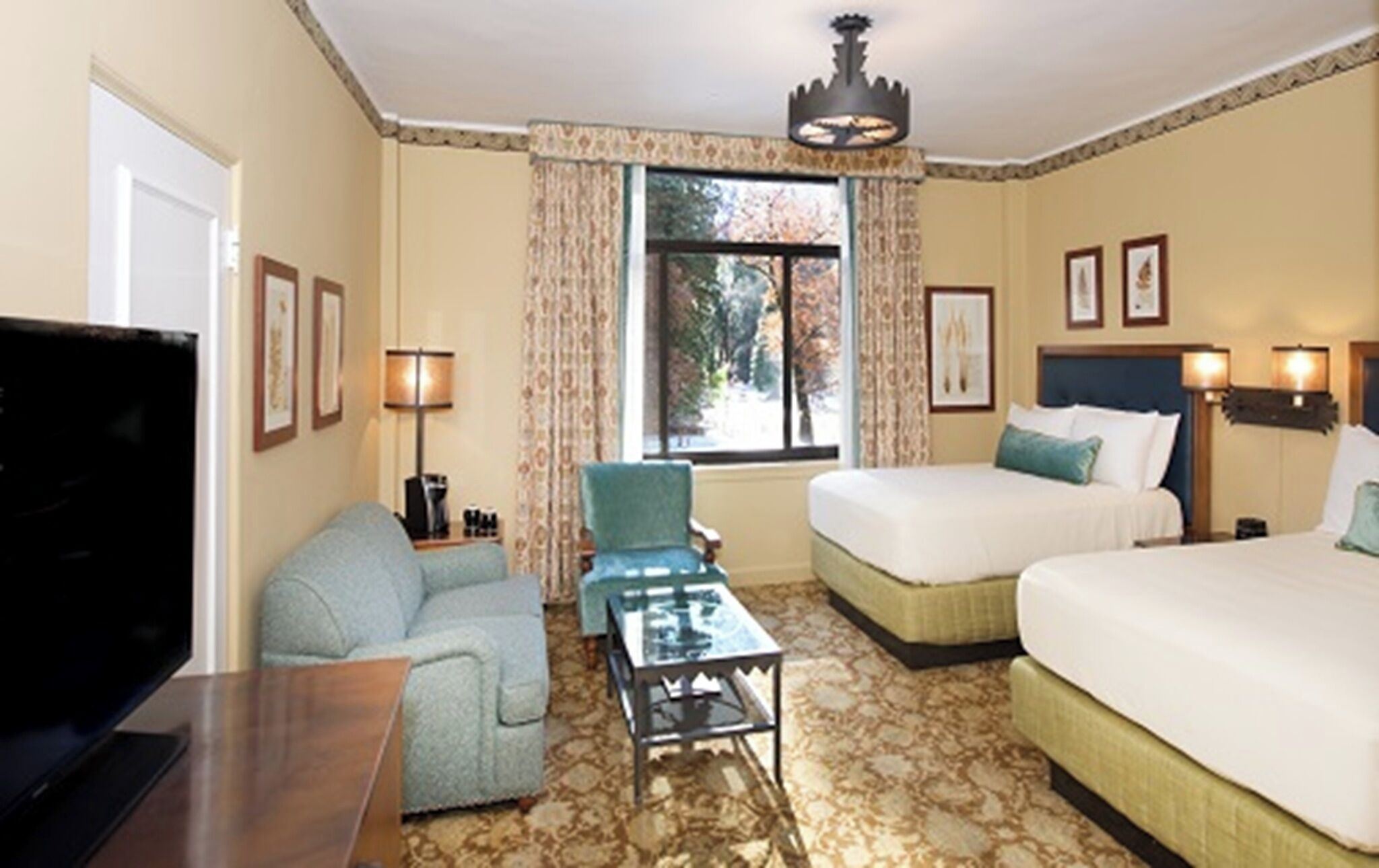 Une chambre d’hôtel avec deux lits, une télévision, une table basse, une chaise et une fenêtre avec des rideaux.