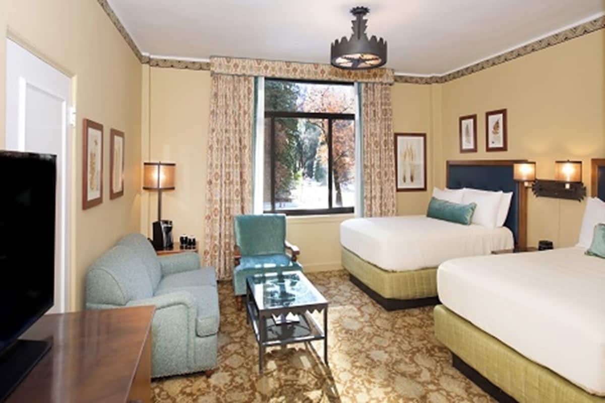 A hotel room with two beds, a TV, a coffee table, a chair, and a window with curtains.