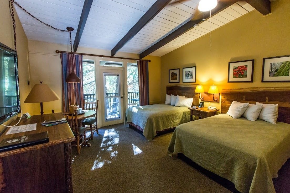 Een hotelkamer met twee bedden, een bureau met lamp, een stoel en een raam met gordijnen.