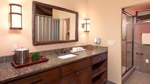 Un baño con encimera de granito, armarios de madera, un espejo grande y una cabina de ducha de vidrio.