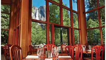 A dining area with wooden tables and chairs, large windows offering a view of a mountainous landscape.