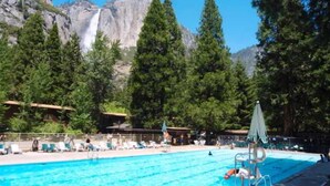 Piscina con montañas al fondo, rodeada de árboles y un cielo despejado.