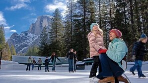 A group of people ice skating in a snowy outdoor setting with a mountainous backdrop. - Curry Village (Yosemite National Park)