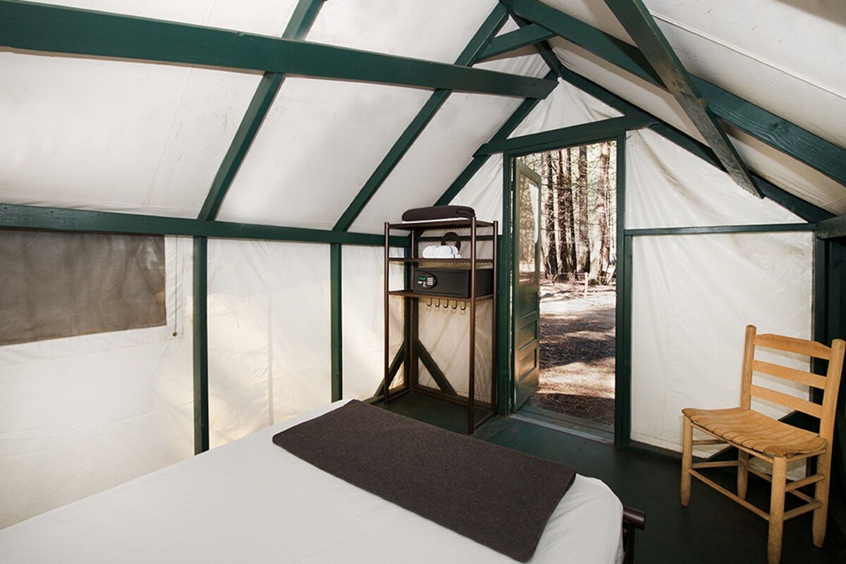 A tent with a bed, a chair, and a small table with a chair.