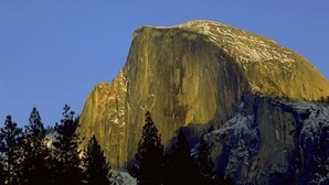 A mountain with a prominent peak, surrounded by trees and a visible moon in the sky. - Curry Village (Yosemite National Park)