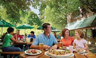 Un área de comedor al aire libre con mesas, sombrillas y un letrero que dice "PIZZA PATIO".