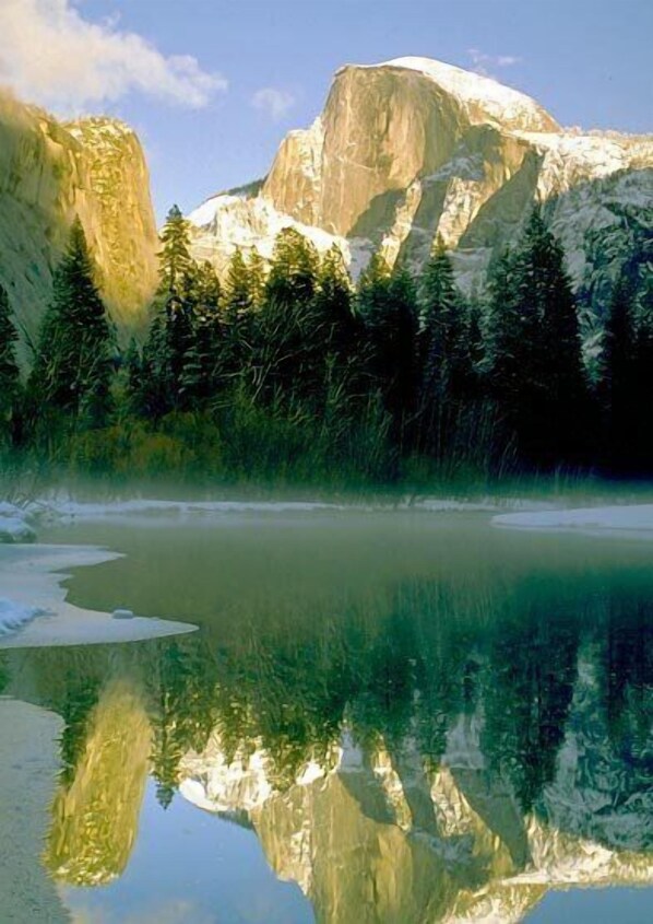 A mountain landscape with a clear reflection in a calm body of water, surrounded by dense forest. - Curry Village (Yosemite National Park)