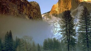 A mountainous landscape with a prominent rock formation and dense forest.