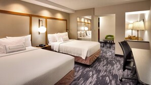 A hotel room with two beds, a desk, a chair, a small table, and a mirror.