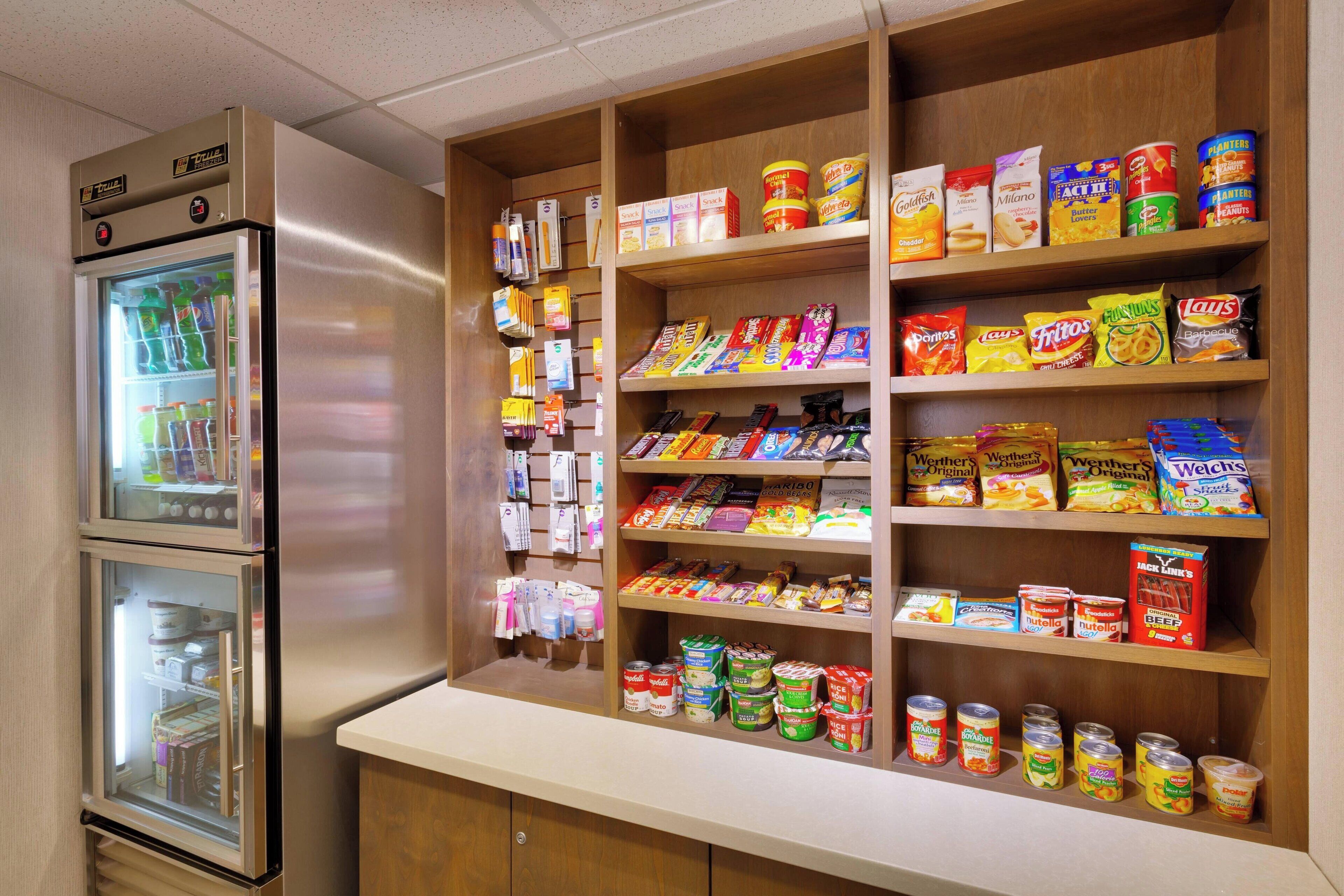 Et område med snacks og drikkevarer, med et køleskab og reoler fyldt med forskellige produkter.