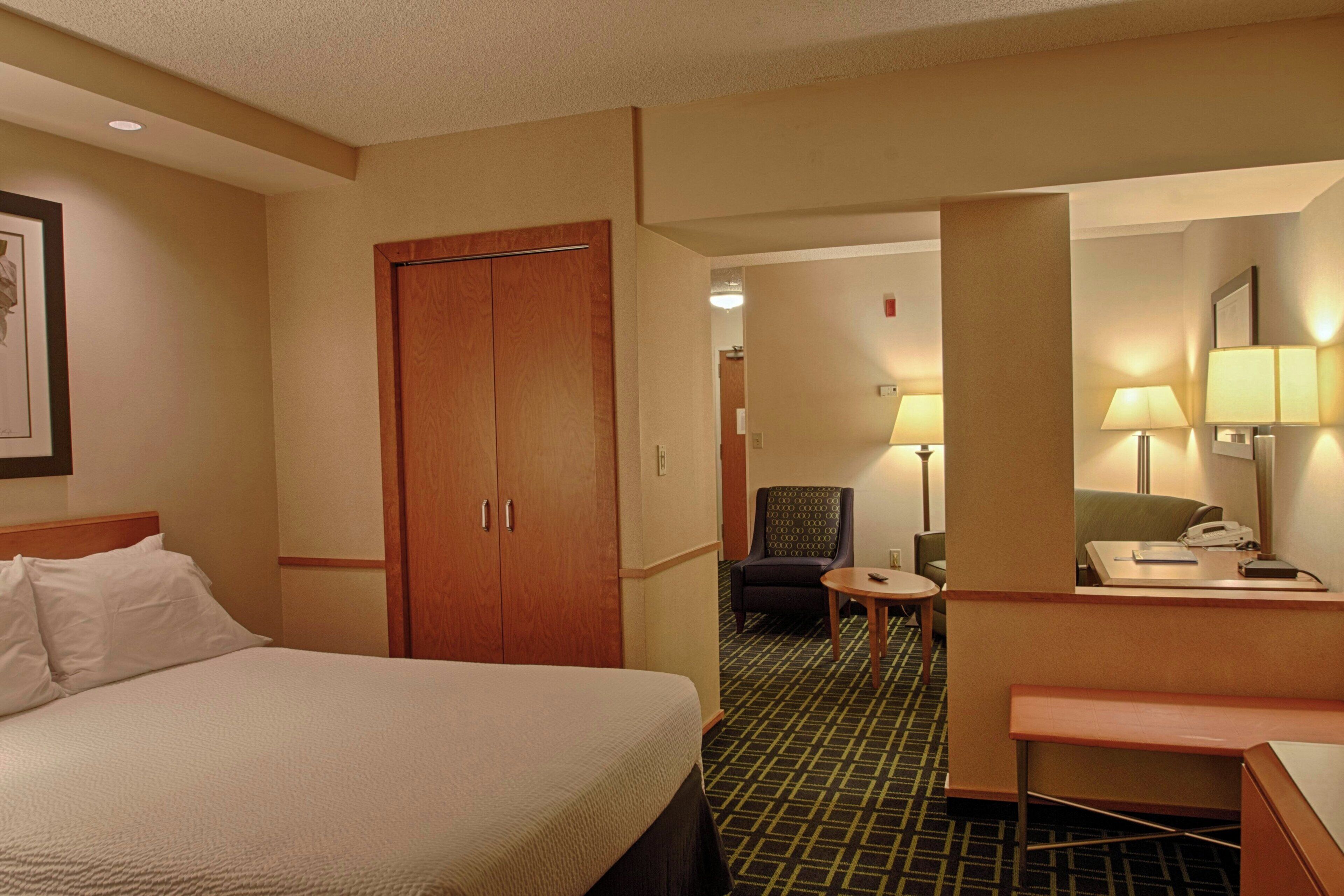 Habitación de hotel con cama, escritorio, silla y una mesita. Hay un espejo en la pared y una puerta que da a otra habitación.