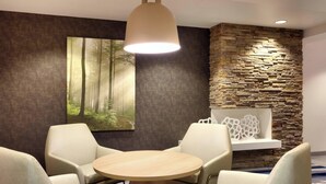 A modern room with a round table and four chairs, a large forest-themed painting, a stone accent wall, and a recessed ceiling light.