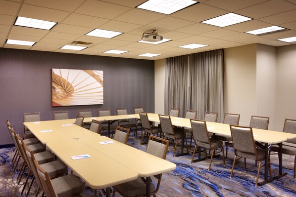 A conference room with a long table, multiple chairs, a projector, and a large window with curtains.