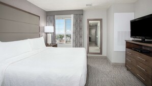 A hotel room with a large bed, a television, a dresser, and a view of the outdoors.