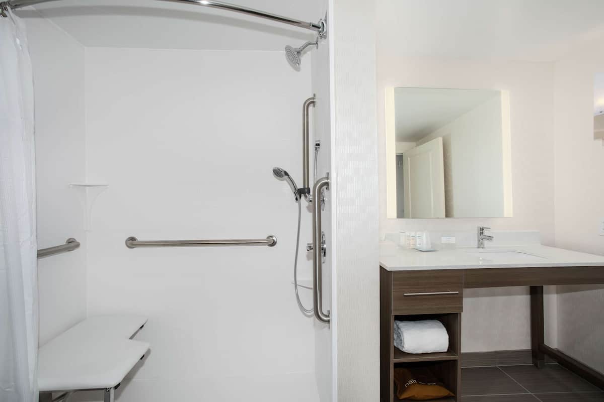 Un baño moderno con ducha, barras de apoyo, lavamanos y espejo.