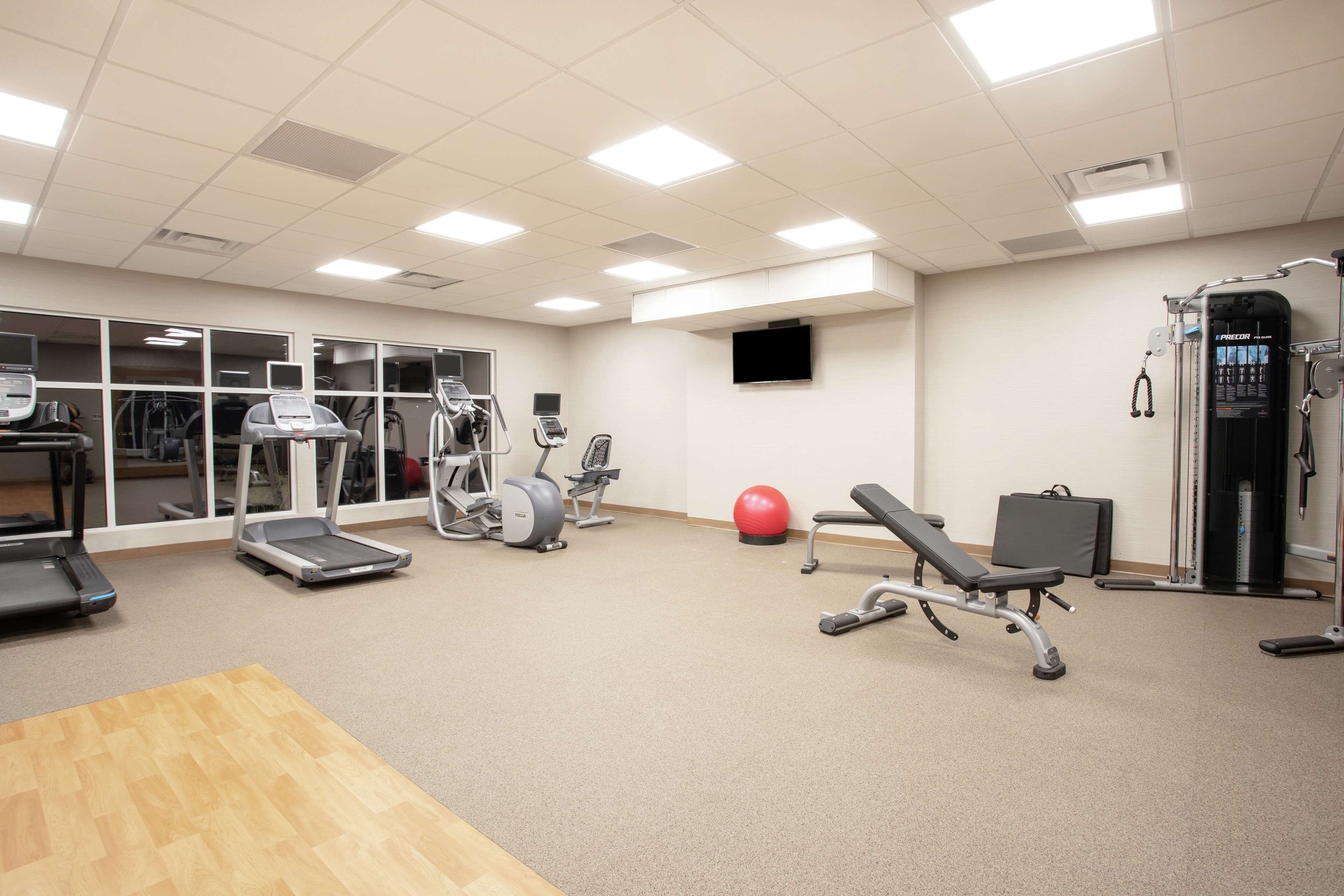 Ein Fitnessraum mit Laufbändern, Crosstrainern, einem Ergometer, einem roten Trainingsball und einer Gewichtbank.