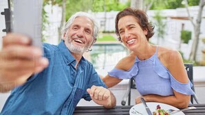 Two people sitting at an outdoor table with a smartphone, a plate of food, and a drink.
