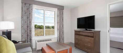 Habitación de hotel con cama, televisor, escritorio con lámpara, calefactor y ventana con cortinas.