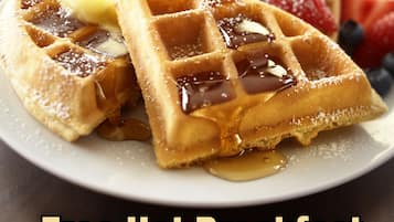 Une assiette de gaufres nappées de sirop et garnies de fruits, et une main versant du sirop.