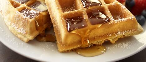A plate of waffles with syrup and fruit, and a hand pouring syrup.