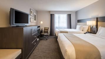 A hotel room with a TV, a desk, two beds, and a window with curtains.