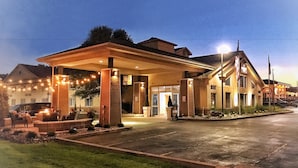 Un hotel con un área de estar exterior cubierta, una entrada bien iluminada y un jardín frontal ajardinado.