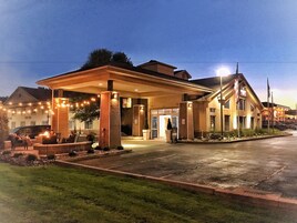 Un hotel con un área de estar exterior cubierta, una entrada bien iluminada y un jardín frontal ajardinado.