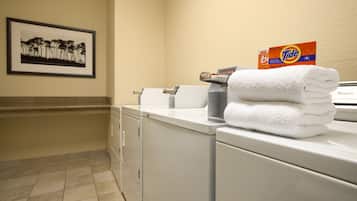 Un espace dédié à la lessive, avec une pile de serviettes blanches, une boîte de lessive Tide et un tableau encadré accroché au mur.