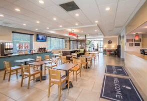Un espacio interior amplio con varias mesas y sillas, una recepción y un mostrador con dispensador de bebidas.