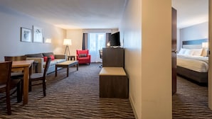 Habitación de hotel con cama, escritorio, silla, sofá, televisión y lámpara.