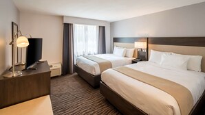 Una habitación de hotel con dos camas, un escritorio con televisor y un ventanal con cortinas.