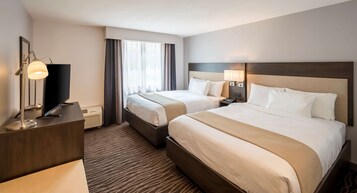 Una habitación de hotel con dos camas, un escritorio con televisor y un ventanal con cortinas.