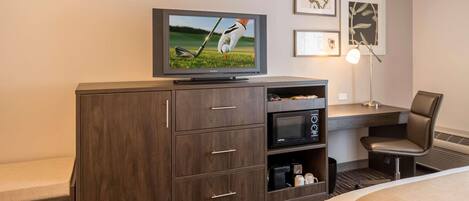 A hotel room with a wooden cabinet, a flat-screen TV, a desk with a lamp, a chair, and a bed.