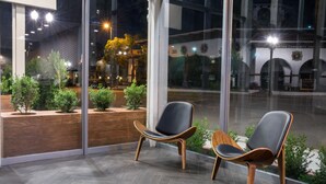 A modern interior with two black leather chairs and a wooden table, large windows offering a view of a courtyard with plants and a building in the background. - Hotel Xilo Glendale (Glendale)