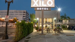 A hotel sign with a modern design, a well-lit entrance, outdoor seating area, and a parking lot. - Hotel Xilo Glendale (Glendale)