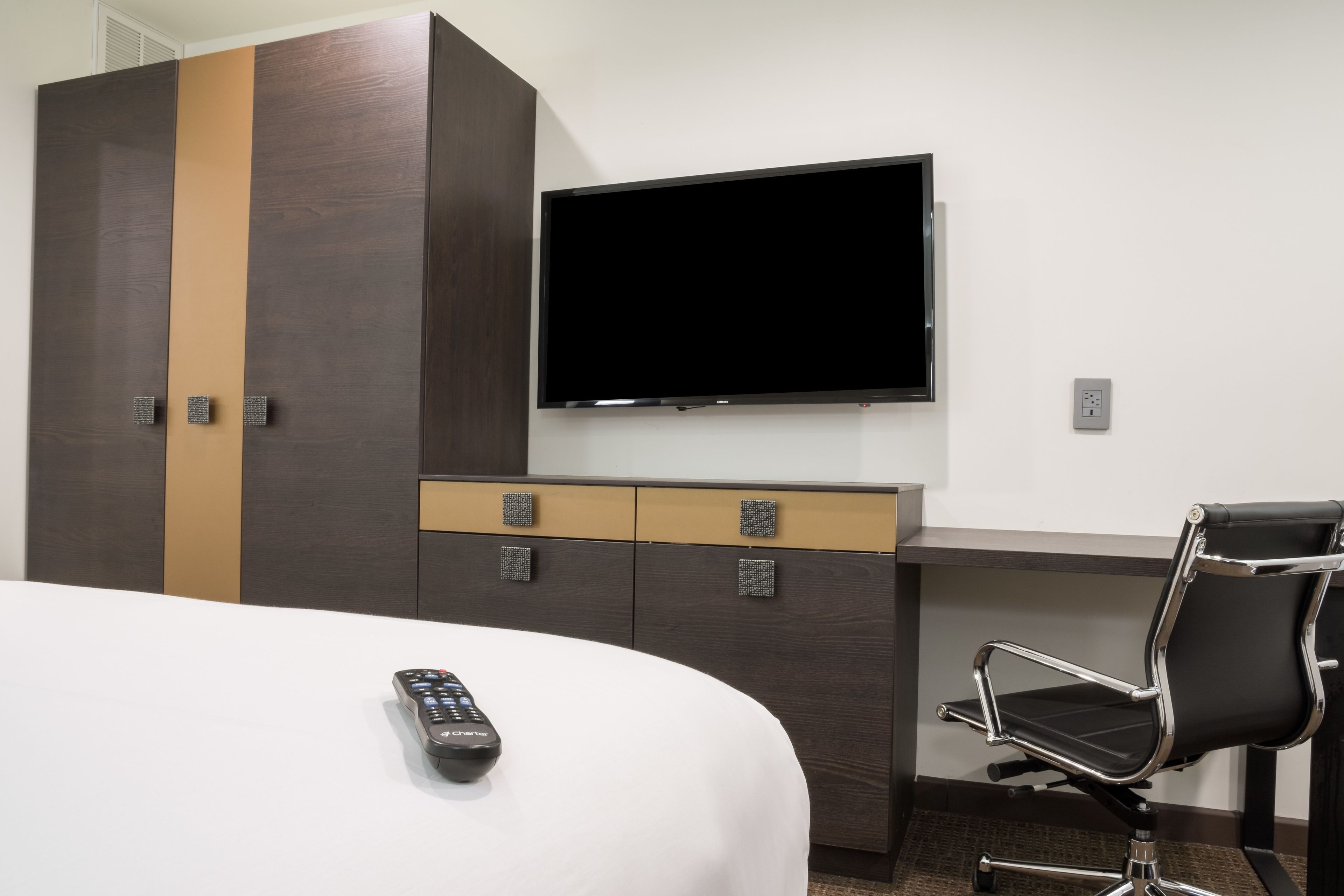 Habitación de hotel con cama, televisor montado en la pared, escritorio con silla y armario.