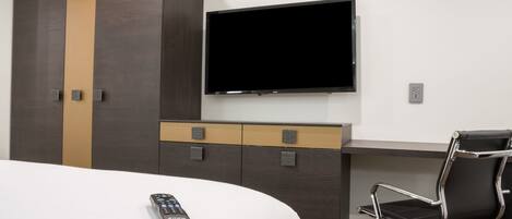 Habitación de hotel con cama, televisor montado en la pared, escritorio con silla y armario.