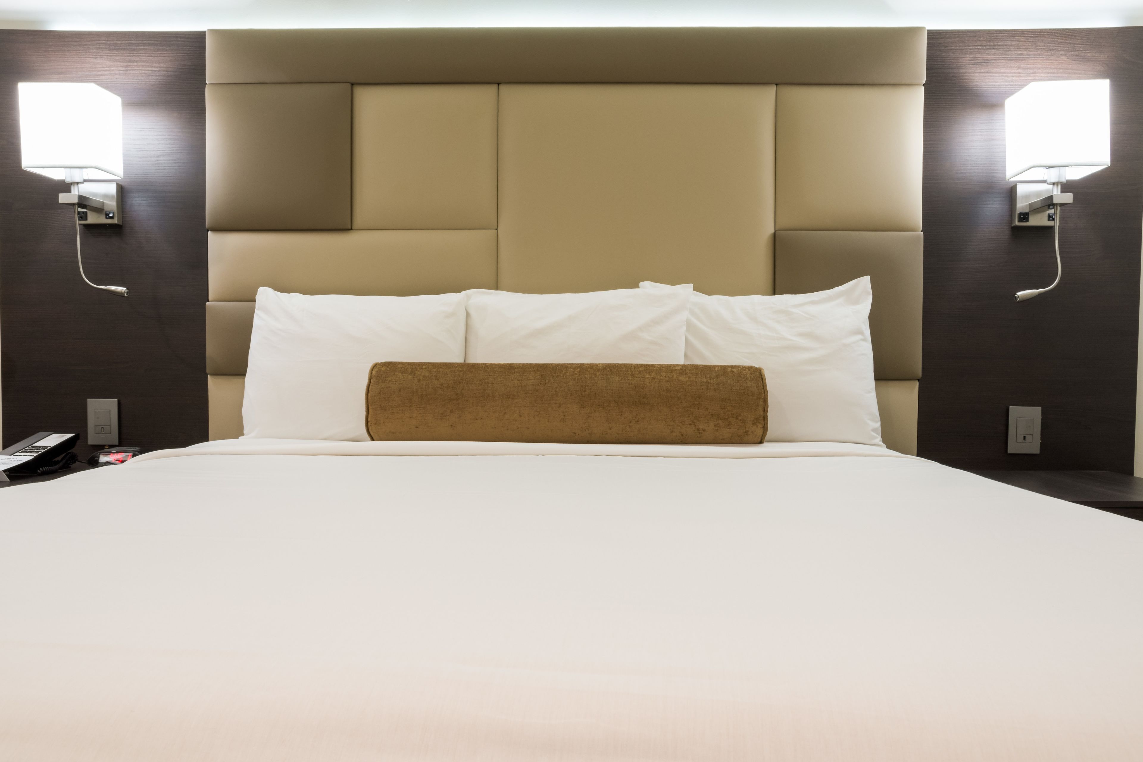 A hotel room with a large bed, a headboard with built-in lighting, and bedside lamps.