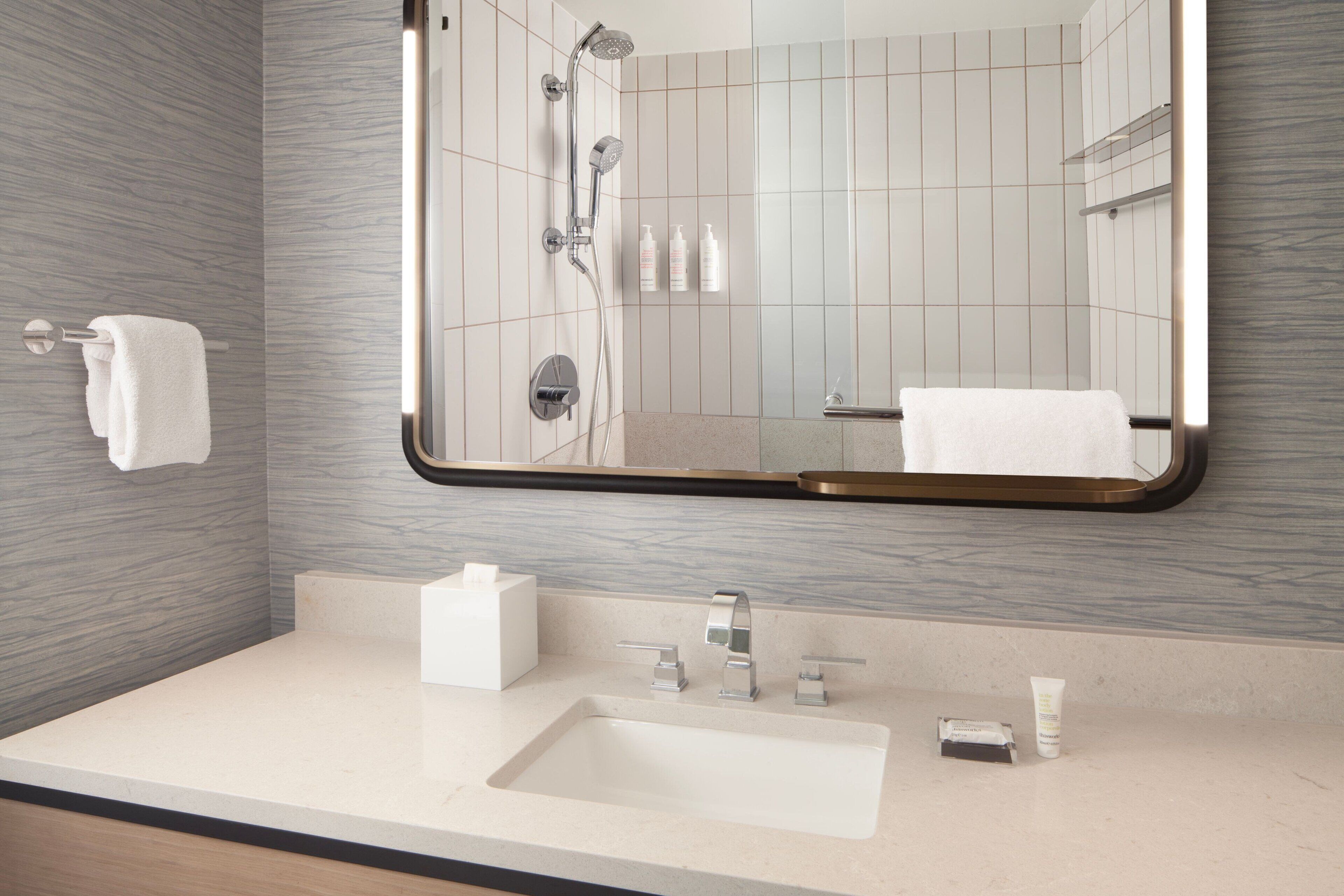 A modern bathroom with a large mirror, a sink, and a shower.