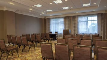 A conference room with rows of chairs, a podium, and large windows with curtains.